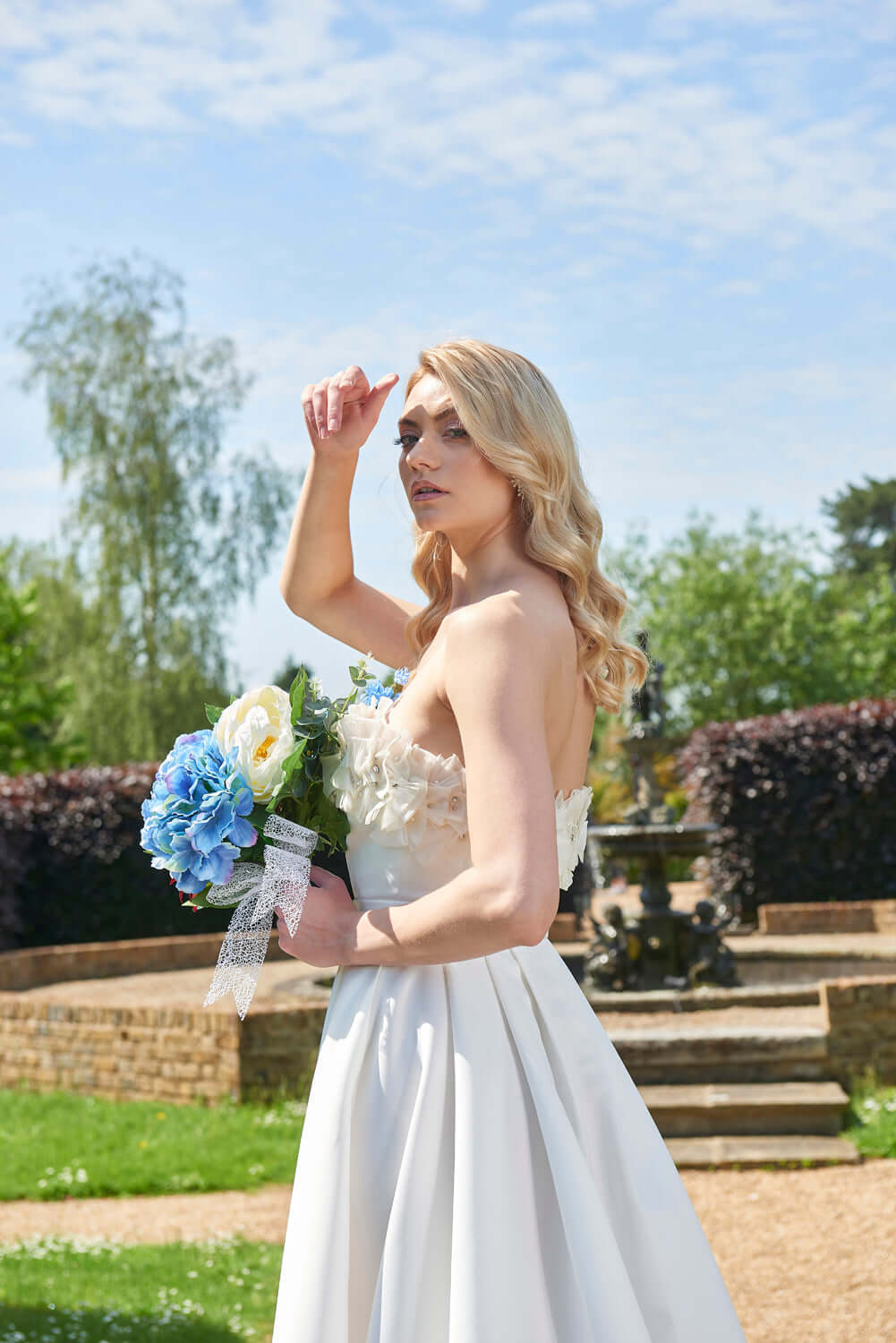 Charming side profile of the Rhea Wedding Dress by Eve Couture London, accentuating its elegant silhouette and stunning details in a natural environment.