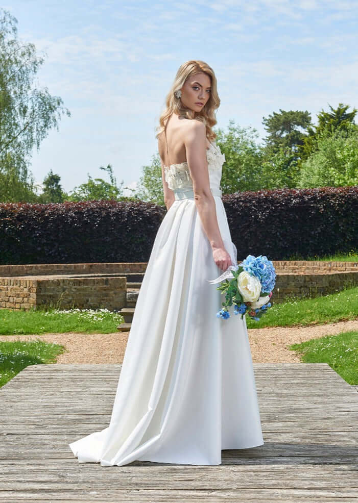 Back view of the stunning Rhea Wedding Dress by Eve Couture London, highlighting its luxurious design and graceful train in a picturesque garden setting.