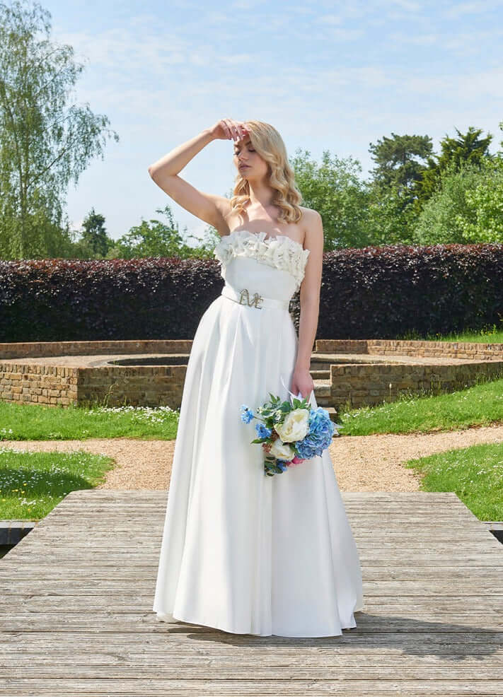 Elegant Rhea Wedding Dress by Eve Couture London, featuring delicate beaded organza flower embellishments, showcased outdoors with a beautiful bouquet.