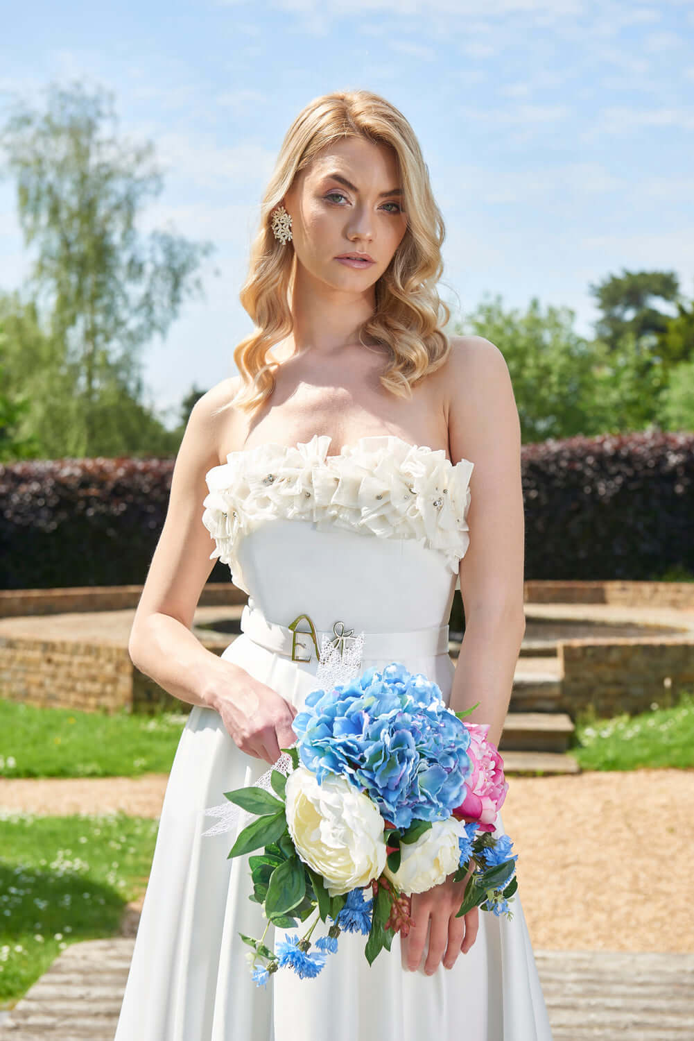 Close-up of the exquisite strapless Rhea Wedding Dress by Eve Couture London, adorned with floral embellishments, complementing a bridal bouquet.