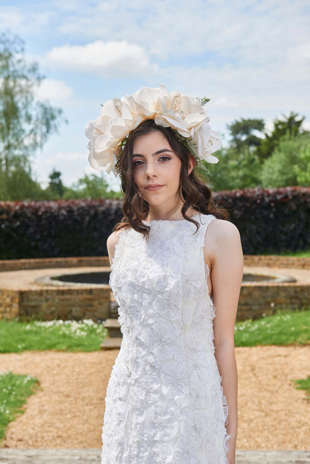 Model wearing Myriss Wedding Dress with 3D floral appliques and floral crown in a garden setting.