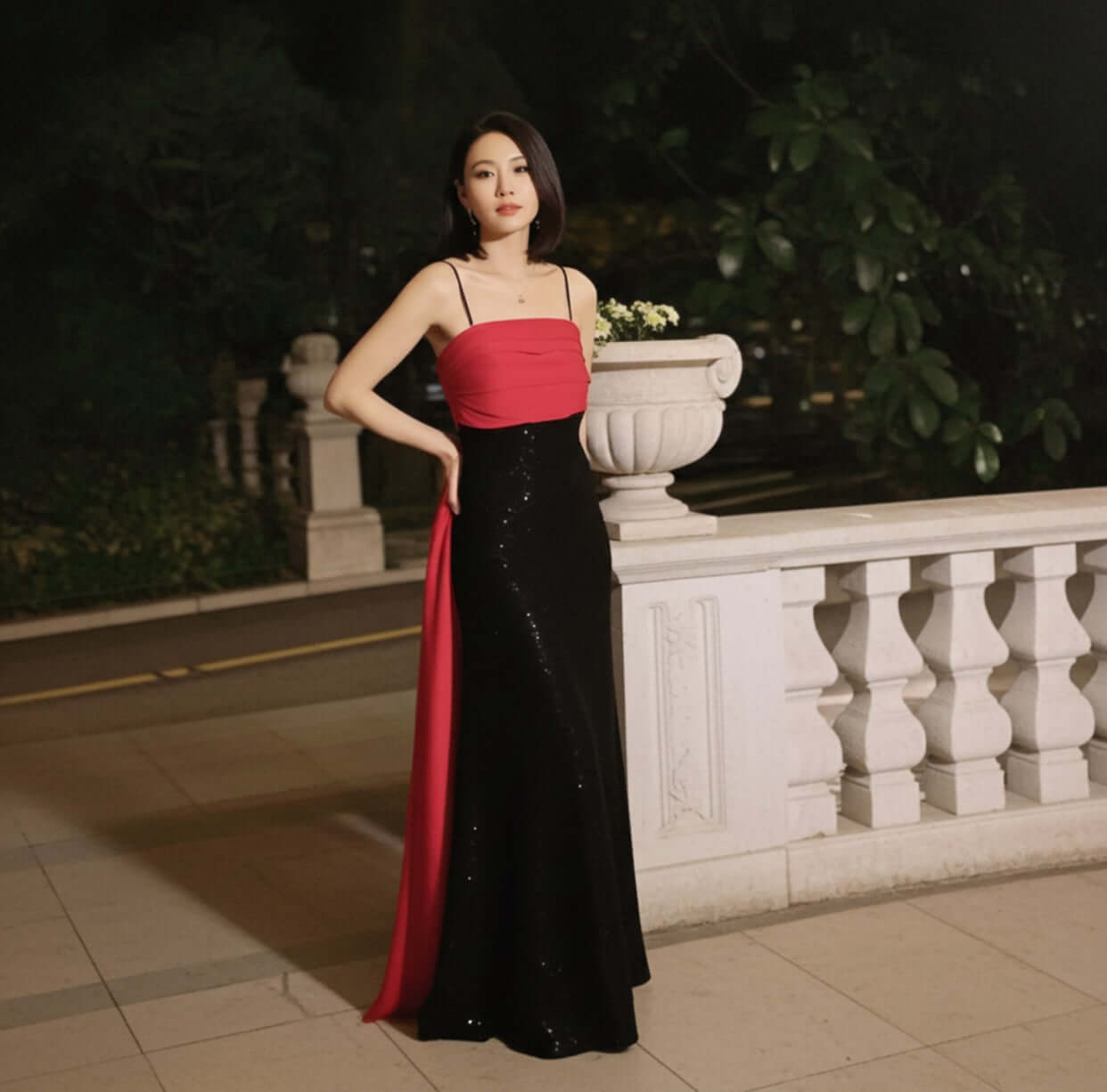 An elegant portrayal of the Amarine Evening Gown by Eve Couture captured outdoors, highlighting the exquisite black sequinned bodice and dramatic red silk organza panel, symbolising luxury and femininity.