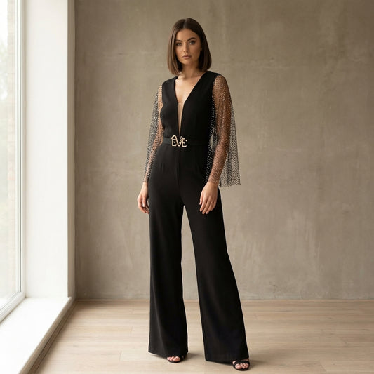 Model showcasing the Anemone Evening Jumpsuit by Eve Couture London, featuring flowy rhinestone mesh sleeves, in a pose that highlights the luxurious black design. This Black luxury Jumpsuit is perfect for elegant occasions, exuding couture charm that makes it an ideal choice for a red carpet look. Hand made in London, this designer evening jumpsuit is a staple of high-end fashion.